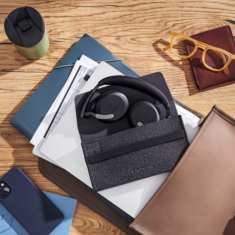 Jabra Evolve2 65 headset neatly stored in its case, on a desk with documents, glasses and smartphone